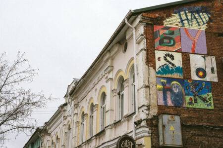 Фасад старовинного будинку з елементами стріт-арту та яскравими малюнками на цегляній стіні.