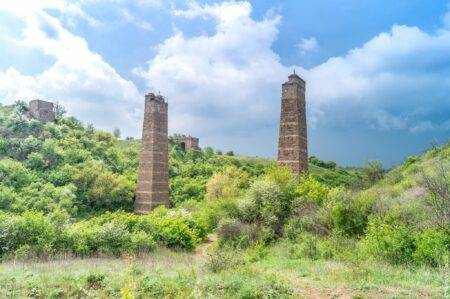 Дві високі старовинні кам'яні колони мосту в квітучій зеленій долині під хмарним небом.