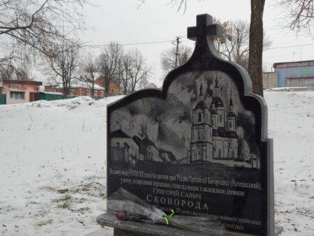 Пам'ятний знак Григорію Сковороді у вигляді кам'яної плити з хрестом та гравюрою храму на тлі засніженого пейзажу.