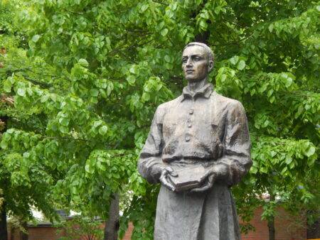 Пам'ятник Григорію Сковороді з книгою в руках на тлі зелених дерев восени або влітку.