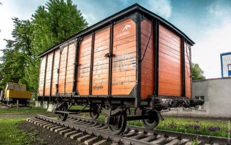 Історичний помаранчевий залізничний вагон на рейках. Експонат з логотипом ArcelorMittal та старими написами.